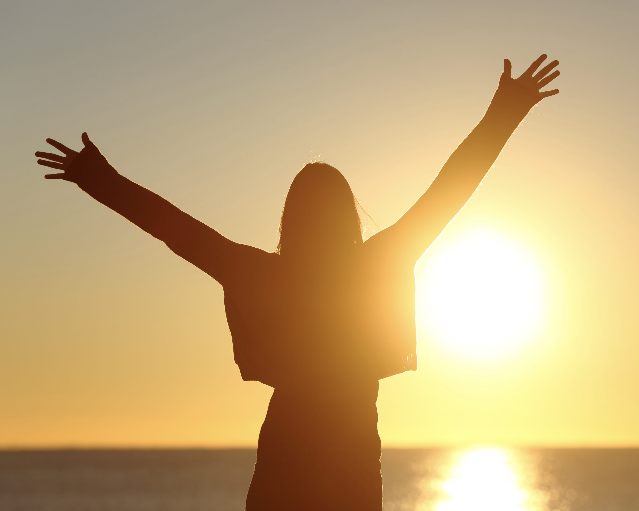 Free woman raising arms watching sun at sunrise